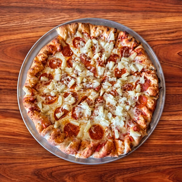 A whole pepperoni and pineapple pizza on a metal pan, centered on a wooden table.