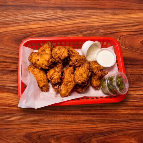 Crispy fried chicken wings in a red basket with ranch and jalapeño dipping sauces on a wooden table.