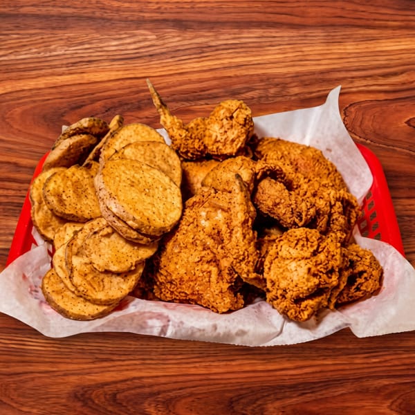 A red basket filled with crispy fried chicken and round, seasoned potato chips on a wooden table.
